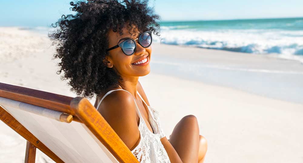 Woman sitting on a beachchair on the beach with sunglasses enjoying the sunlight